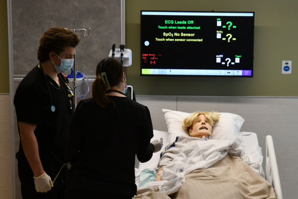 Two students work with a patient manikin in simulation suite.